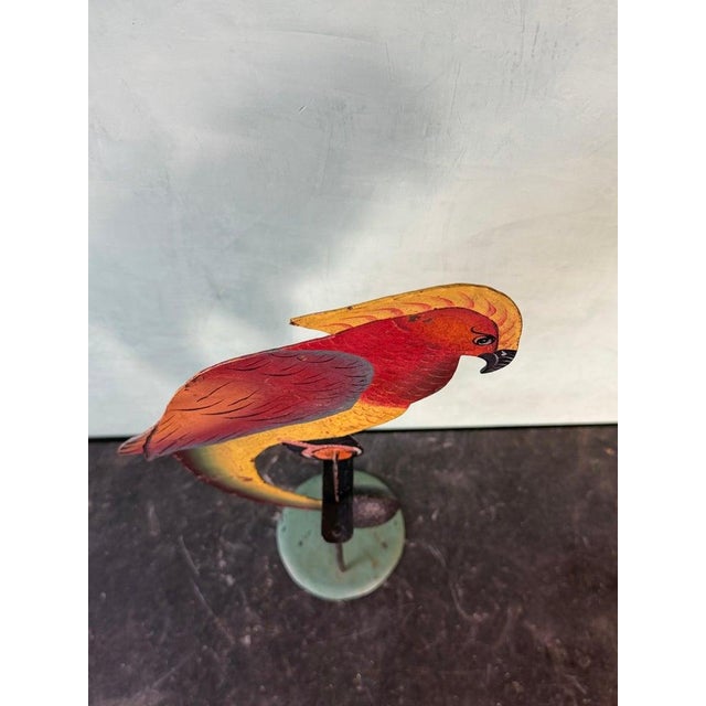 A vibrant vintage folk art kinetic sculpture depicting a stylized parrot perched in a graceful curved form. Crafted in...