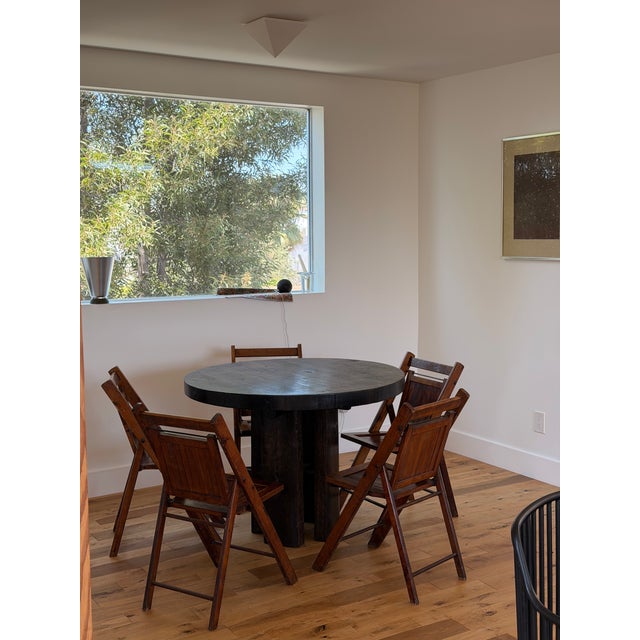 A sculptural round table crafted from richly aged, dark timber. The substantial tabletop showcases natural wood grain,...