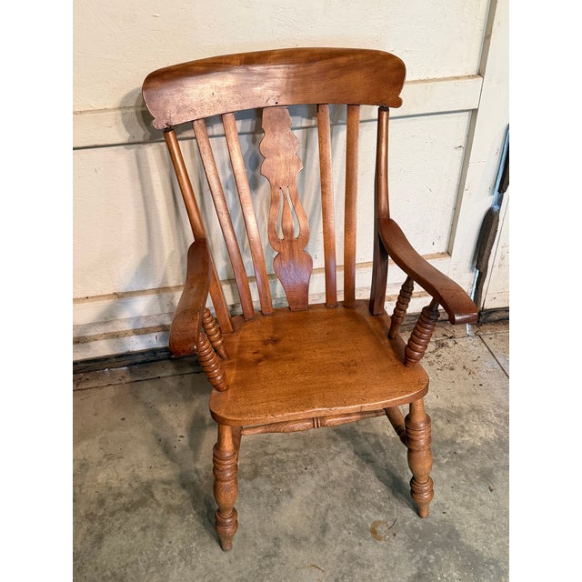 Antique walnut armchair featuring a carved backrest with a central decorative splat. The chair includes turned spindle arm...