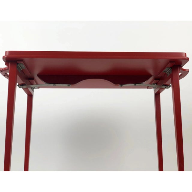 A folding, wooden tray table in burnt orange colour, from the 1930s. The tray uses a simple mechanical mechanism composed...