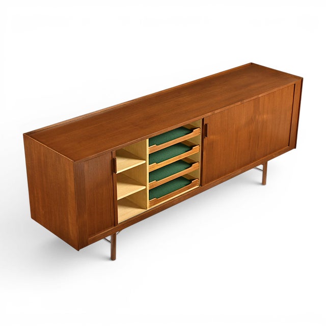 Designed by Ib Kofod-Larsen for Brande Møbelfabrik, this exceptional teak sideboard showcases the refined structural...