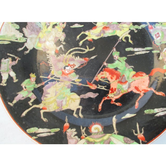 Chinese Famille Noire hand-painted plate. Elaborately dressed and armored warriors charge on horseback. Banners, tents,...