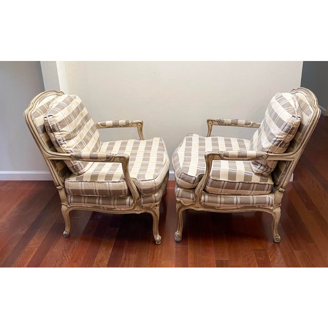 A pair of French Provincial style bergère chairs in a traditional neutral plaid. Original upholstery with high quality...