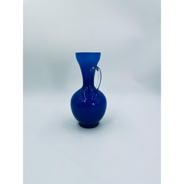 A decorative vintage vase made of high-quality glass. The vase is a deep cobalt blue, hand-formed in the shape of a jug...