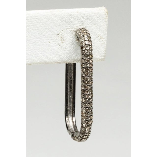 An unusual pair of hoops in a rectangular shape set in an oxidized sterling silver with round, brilliant cut diamonds in a...