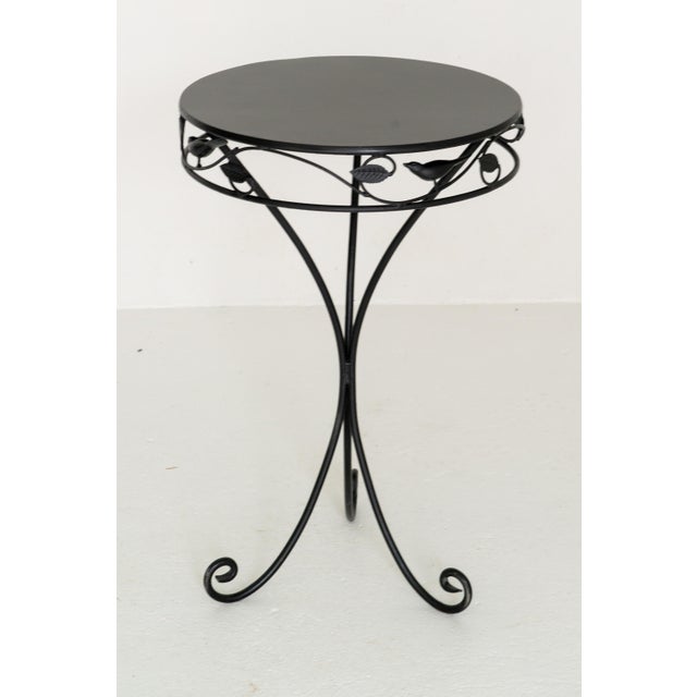 An unusual small round garden side table in black. The table apron is decorated with leaves and three dimensional birds.