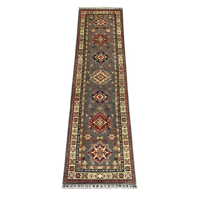 A Kazak-style wool runner with a charcoal gray field and a repeating row of tribal medallions. The cream patterned border...