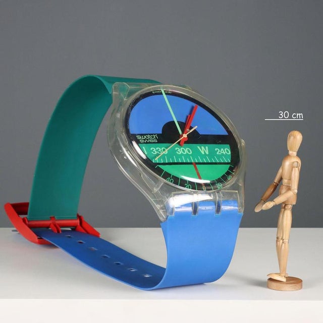 Maxi Swatch Nautilus wall clock. The dial depicts a flying horizon with blue, green, and white details, accompanied by...