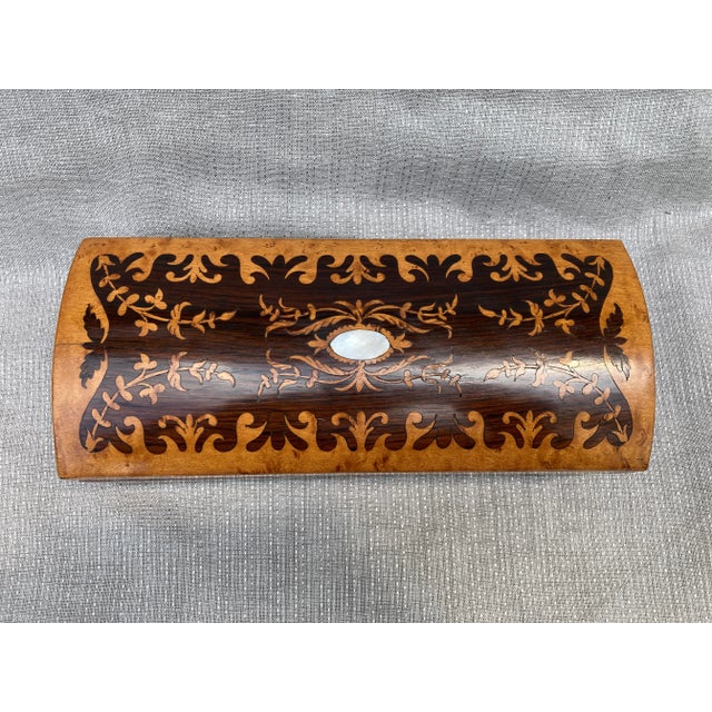 Small lidded marquetry box with mother of pearl accents. Lined in a marbled paper. Hinged at the back, with green felt...
