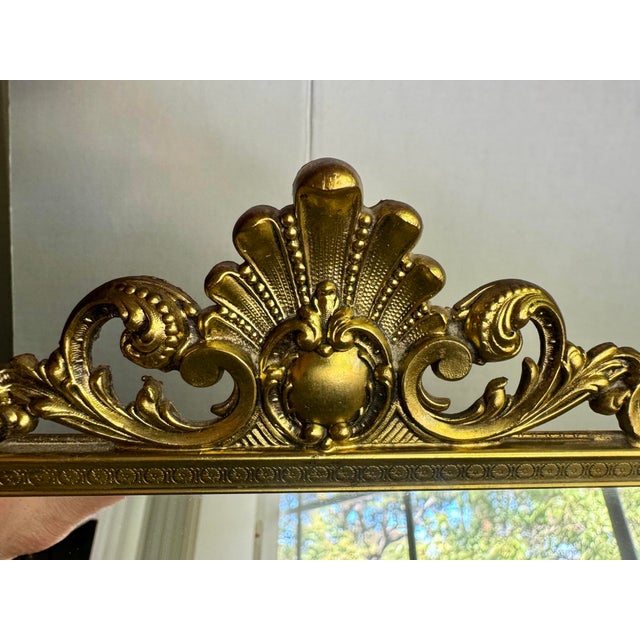 A glamorous mid-century vanity mirror framed in gilt cast metal. Open Rococo scrollwork, curling acanthus leaves and a...