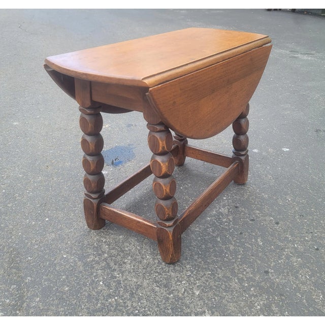 An Early 20th Century Jacobean Low Oak Drop-Leaf Side Table. Measuring 25 inches in diameter with leaves up. Table is...