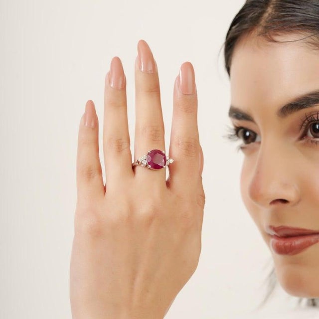 Featuring an 11 mm round-cut ruby weighing 7.2 carats, accented with 0.3 carats of diamonds, this 925 Sterling Silver ring...