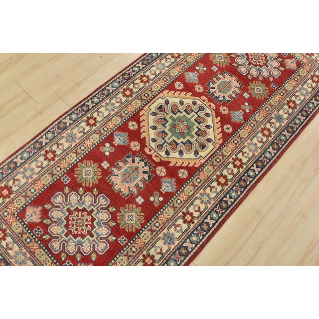 A tribal Caucasian Kazak runner hand-knotted with fine wool on a cotton foundation. This rug has geometric medallions...