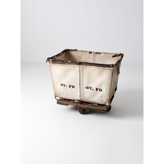 This vintage Dandux industrial laundry cart, from the early 20th century, features a canvas basket with a metal frame and...