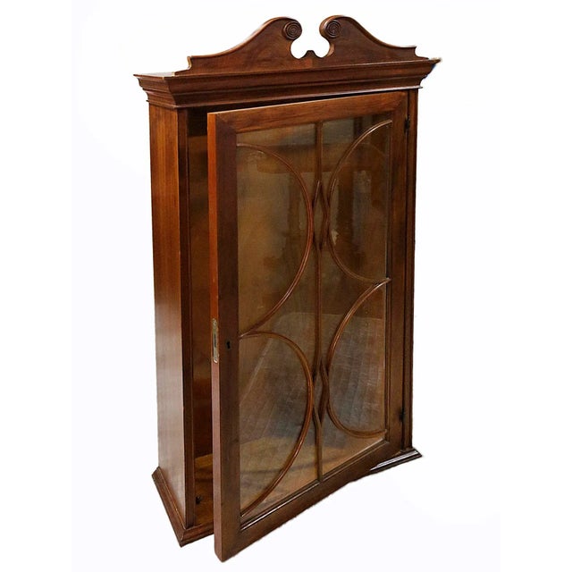 Vintage wooden wall cabinet with decorative glass door, broken arched pediment, dentil molding.