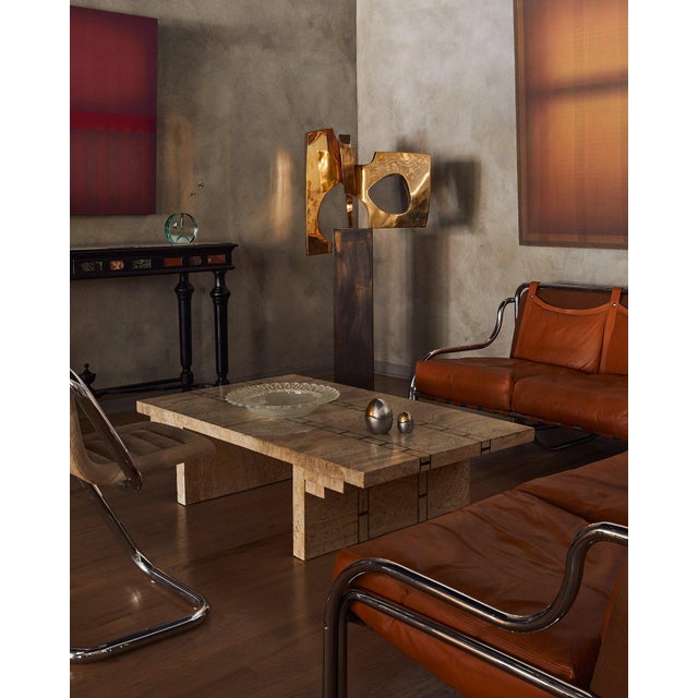 A 1970s Italian coffee table clad in travertine veneer, with inlaid brass detailing. Its broad, rectangular surface is...