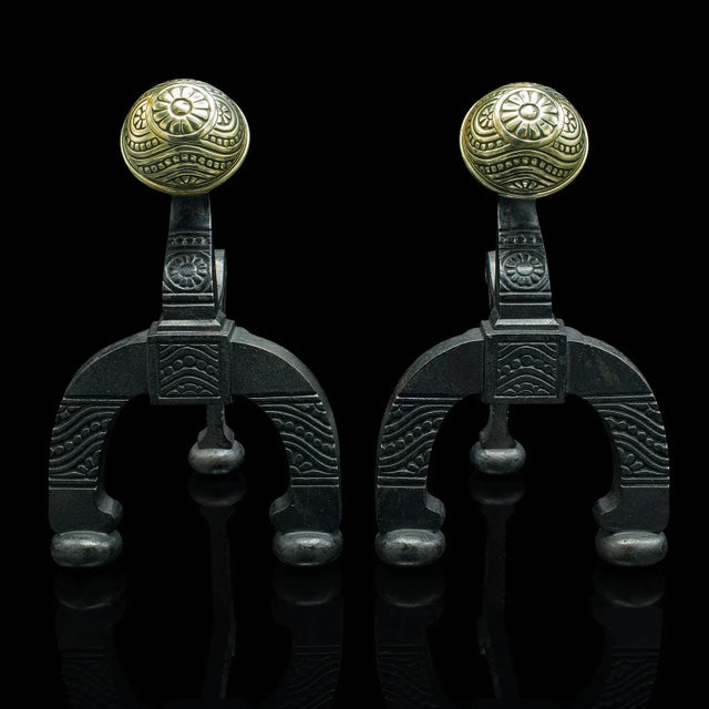 This is a pair of antique decorative firedogs. An English, cast iron and brass fireside andiron in the manner of Thomas...