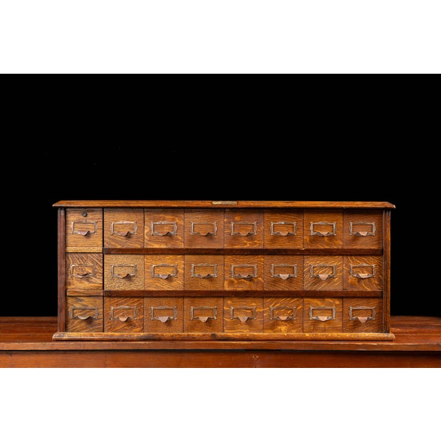 Oak multi-drawer cabinet with brass label hardware. This early 20th-century cabinet features 24 uniformly sized drawers...