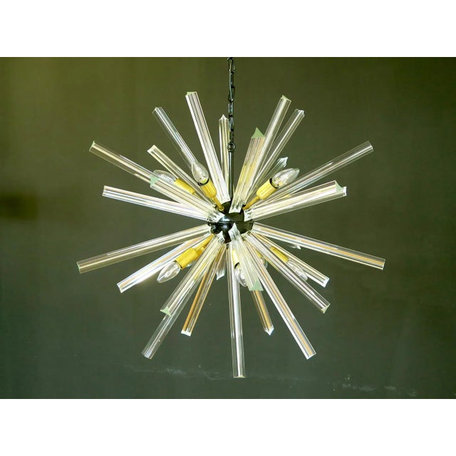 Sputnik chandelier surrounding 30 crystal glass 'triedri' prisms radiating from a center black metal nucleus. Brass lamp...
