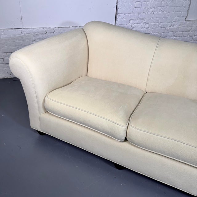 The large three-seat sofa is upholstered in a light butter-tone chenille fabric, with curved back and rolled arms flanking...
