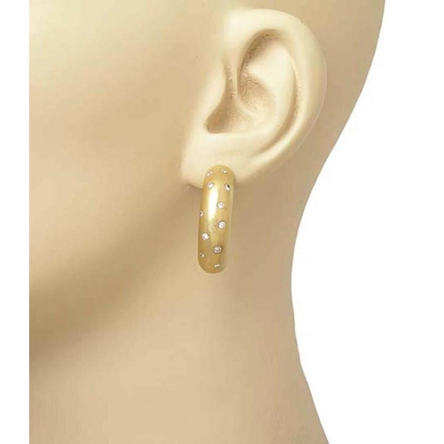 The product is a pair of curved diamond bar earrings made of 18k yellow gold. These huggie earrings are part of fine...