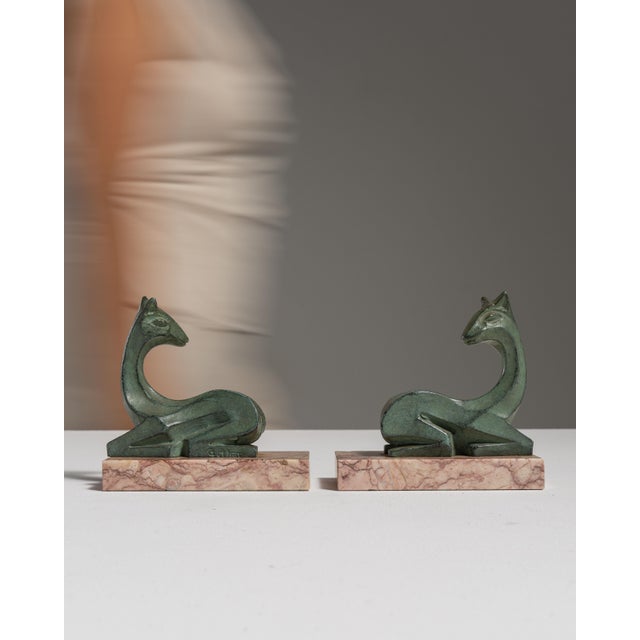 This pair of 1920s Art Deco signed figures on marble bases from France, patinated in green bronze, gazelles resting on...
