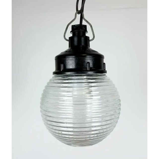 Vintage industrial light made in former Soviet Union during the 1970s. It features a brown bakelite top and a ribbed glass...