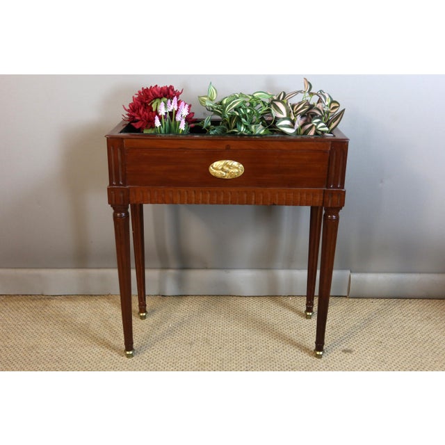 A Louis XVI style mahogany and mahogany veneer jardinière, decorated with truncated fluting, rests on four tapered, fluted...