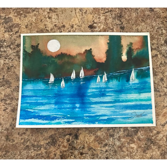 An atmospheric original watercolor painting depicting sailboats gliding across shimmering blue waters under the glow of a...
