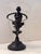 This decorative piece features a clear glass vessel mounted on a bronze pedestal base, adorned with a detailed cherub...