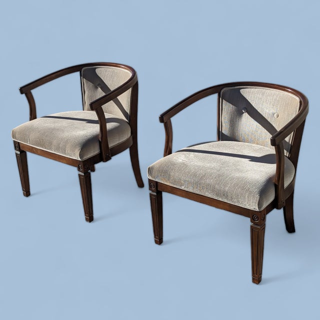 A handsome pair of vintage armchairs with gracefully curved wood frames, wraparound arms, and tailored neutral upholstery....