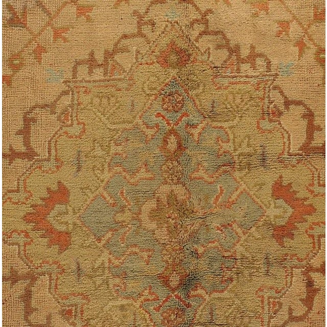This antique Oushak rug boasts a soft peachy-red central field, encircled by a splendid border in soft greens adorned with...