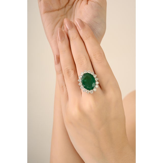 This luxurious cocktail ring showcases a certified 13.17 ct oval-cut emerald, surrounded by a 3.39 ct sparkling halo of...