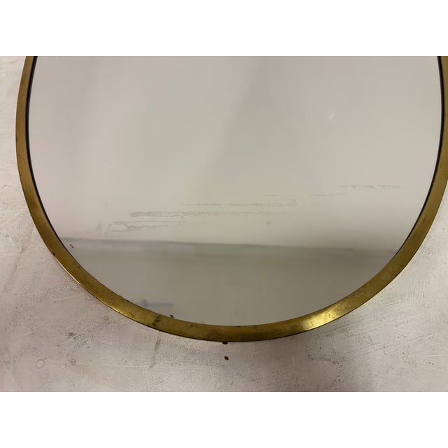 A sculptural Italian shield-shaped wall mirror, dating from the 1950s, featuring an elegant brass frame with softly...