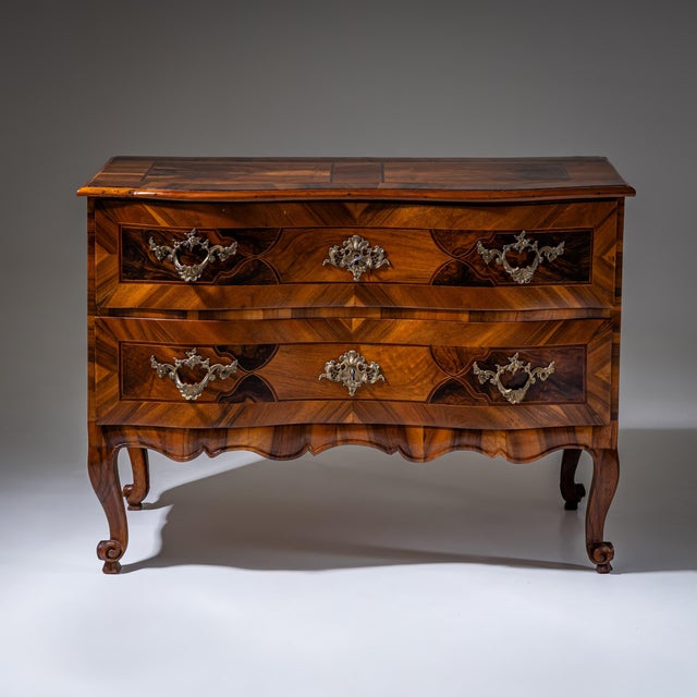 Baroque commode standing on graceful volute legs, featuring a shaped apron and serpentine front. It offers two drawers...