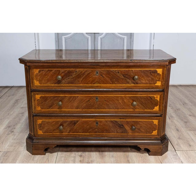 An Italian walnut and ash three-drawer commode from circa 1690 with inlaid décor, canted side posts and ogee bracket feet....