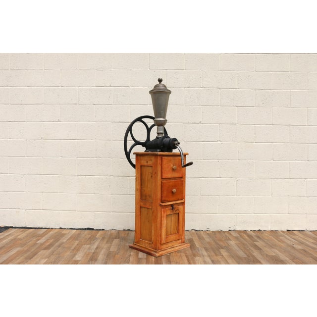 Wonderful antique standing coffee grinder featuring a large cast iron flywheel, hand-crank mechanism, and rustic solid...