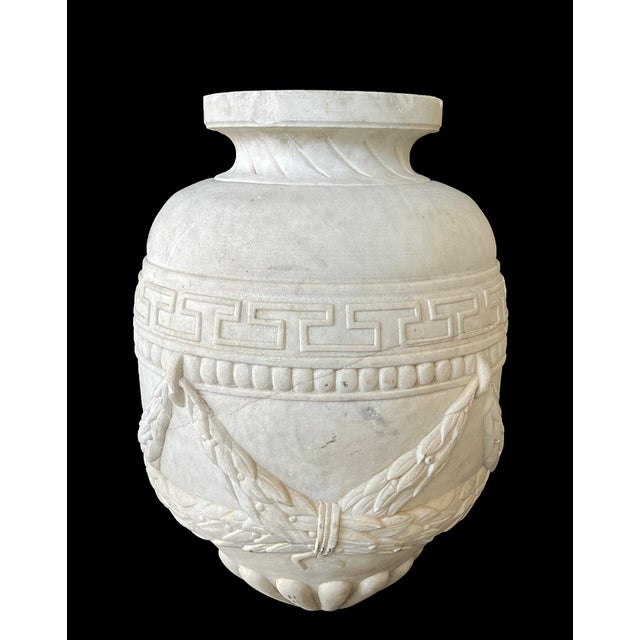 the hand-carved, solid marble urn in the classical taste with short everted neck above a tapering body adorned with relief...