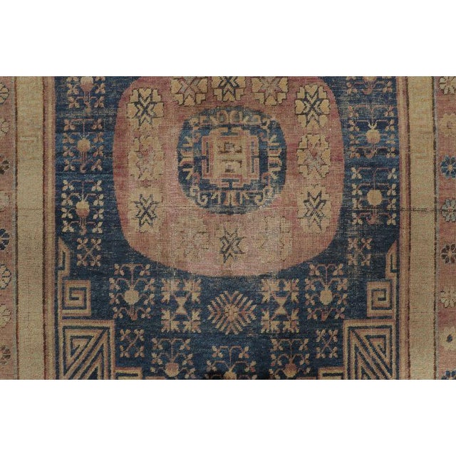 This 6x10 antique Khotan rug, hand-knotted in wool circa 1920–1929, features two geometric medallions on a deep indigo...