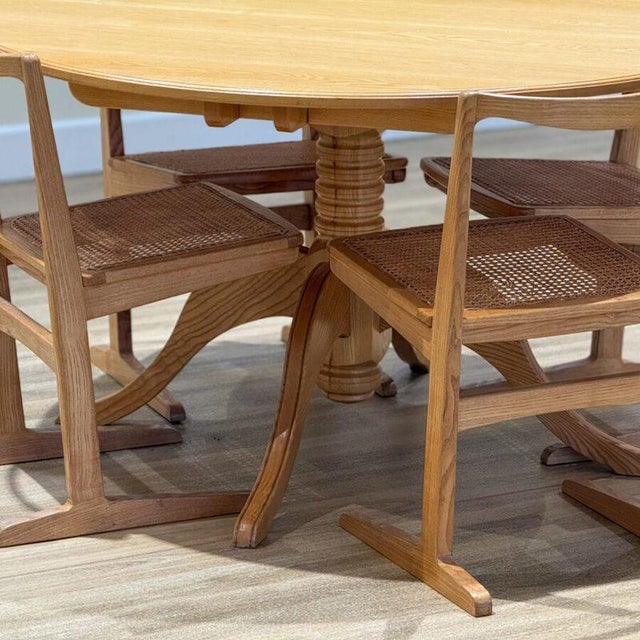 A refined mid-century dining set comprising a circular elm table and four matching rattan chairs, preserved in its...