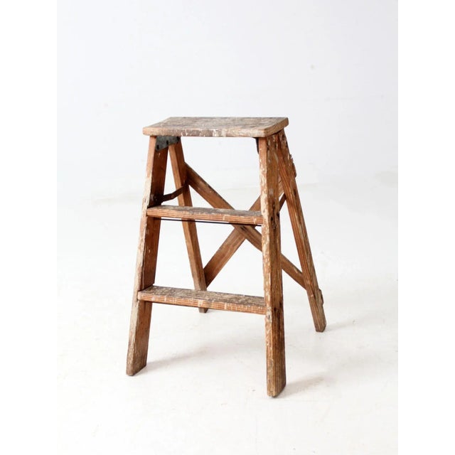 This vintage wooden step ladder features two steps and a rustic finish with old white paint splatters that add aged...