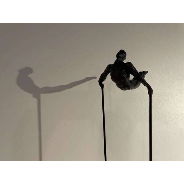 Cast in bronze, an athlete showcasing an athletic feat frozen in mid motion. Mounted on a black granite base. Companion...