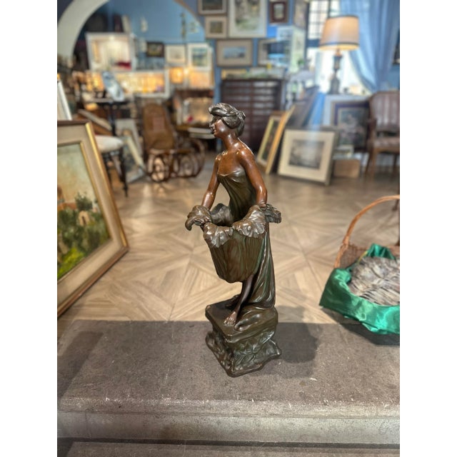 Elegant sculpture depicting an Art Nouveau female figure wearing a soft dress and holding a basket