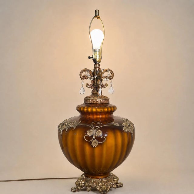 This large vintage brown glass urn table lamp features ornate gold-tone cast metal and hanging clear glass prisms. It...