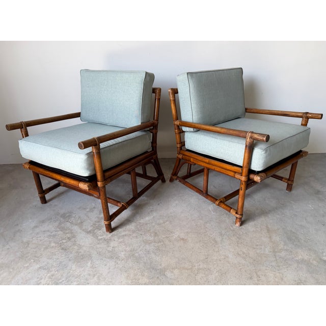 A beautiful pair of vintage rattan bamboo lounge chairs featuring sturdy bamboo frames with wrapped rattan and cushions. A...