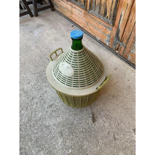 A large green glass Demijohn wine bottle encased in a plastic basket from Farmhouse in Hungary.
