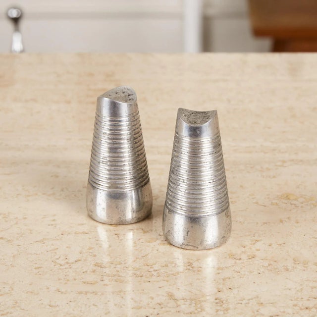 Pair of salt and pepper shakers by Lunt Design Works. The pair feature tapered bodies with a horizontal striated pattern...