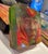 This artwork features a layered composition that reveals a contemplative face, blending vibrant hues of green, red, and...