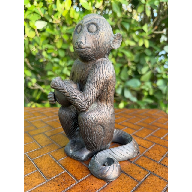 Vintage cast metal monkey sculpture holding an orb with its tail wrapped around the base. Finished in a dark patina with...