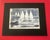 An evocative monochromatic maritime painting depicting a fleet of white-sailed boats moving across a lively, textured sea....